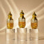 Three gold perfume bottles with floral and fruit decorations on a reflective surface. with a name plat in front f bottle stating "Dunhill Desire", "One Million", and "Ameer Ul OUD".